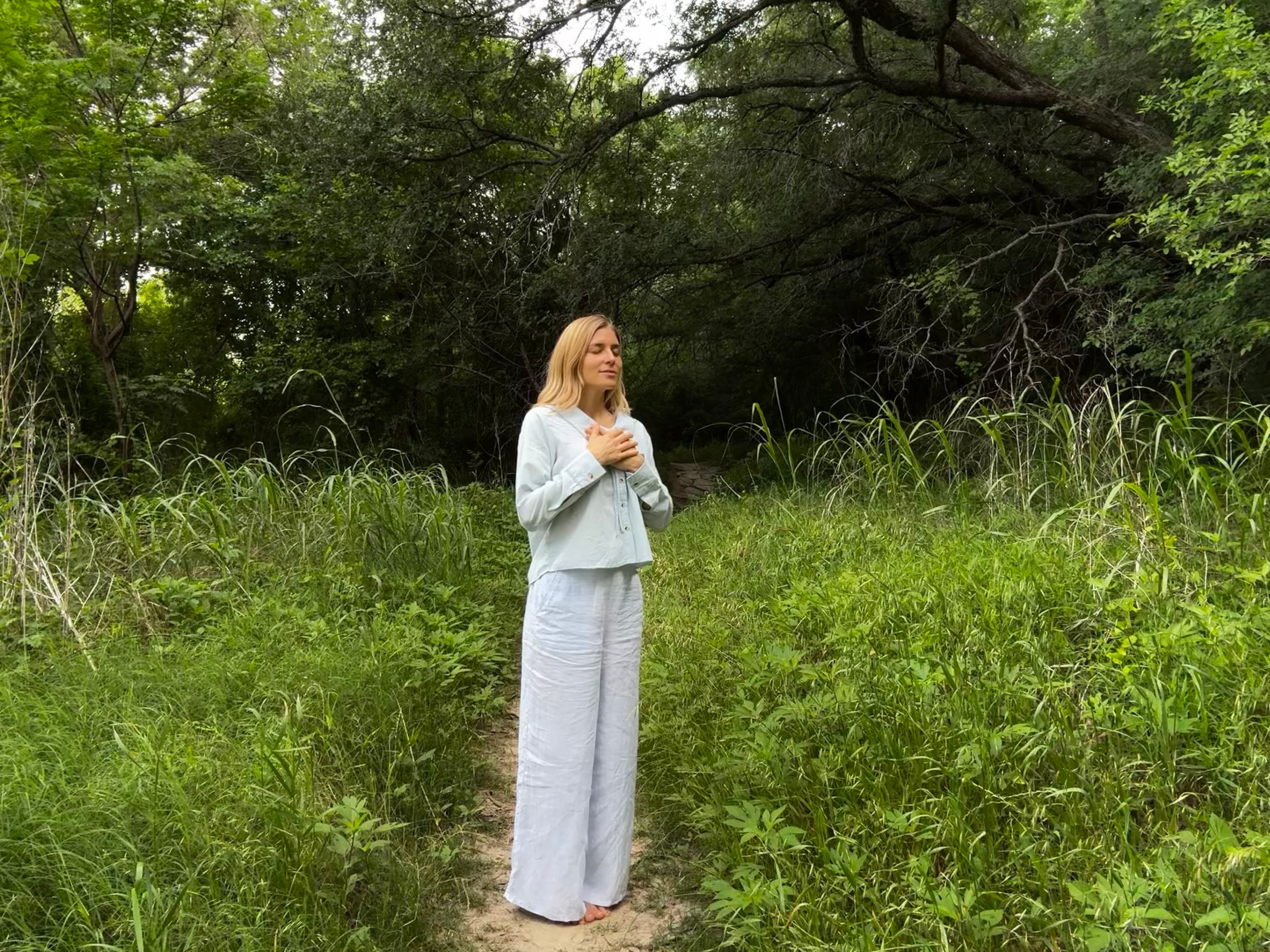 Ashlee Sunshine standing peacefully in a lush green forest